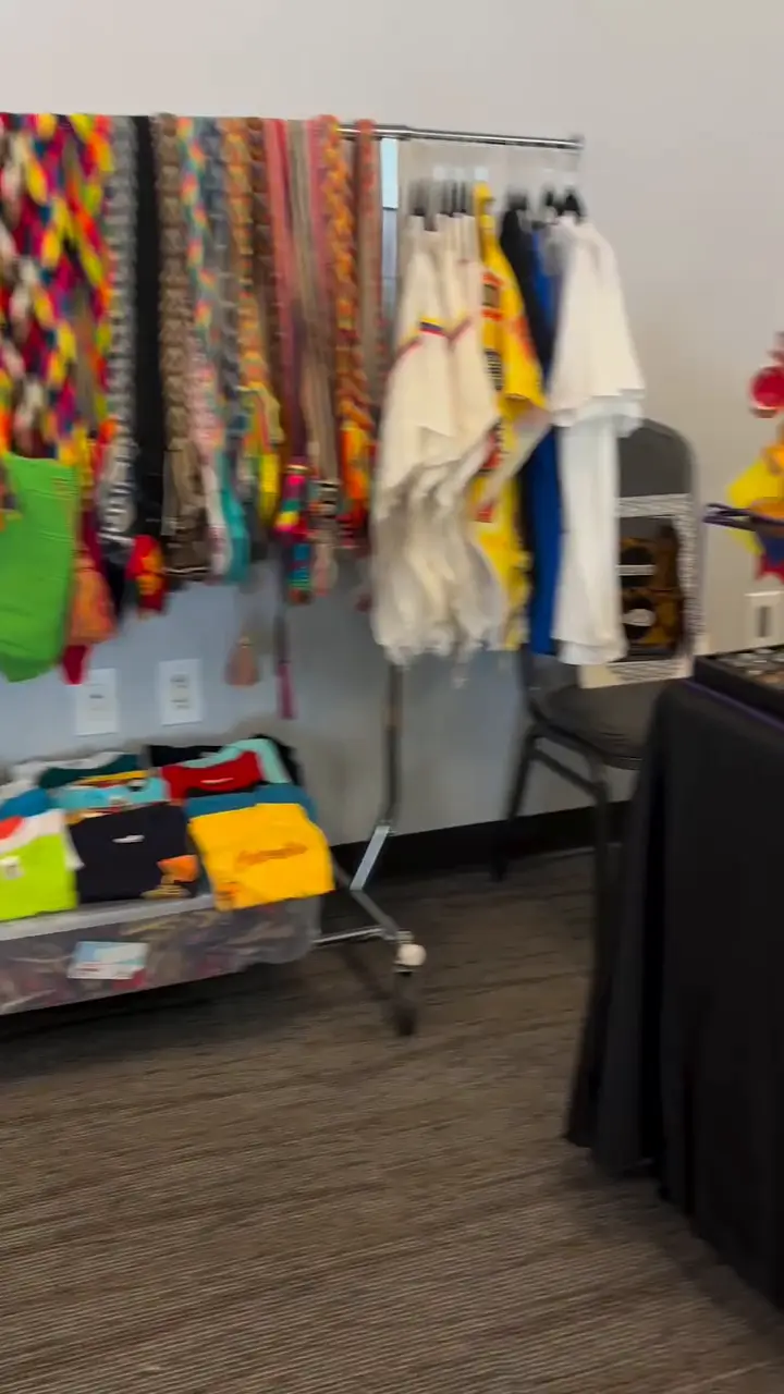 Perchero con tejidos de colores y prendas blancas tradicionales junto a una mesa de artesanías